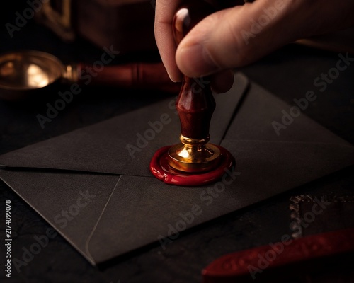 Close-up of Hand Stamping Black Envelope with Red Wax Seal