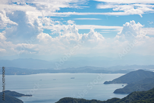 Small ship convoy sails coastal waters by mountainous coast under fluffy clouds on sunny day