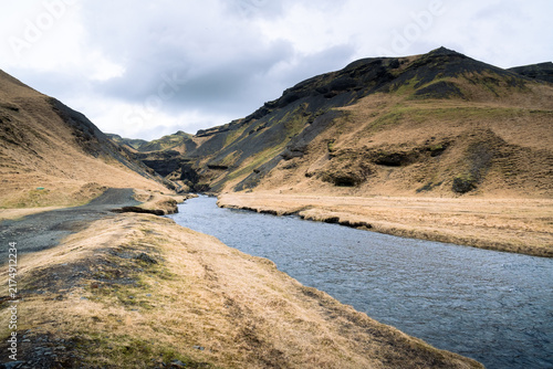 Kvernuholsa River winding through a rocky gorge and yellowed grass in Iceland in the Skogar area during a cloudy day.