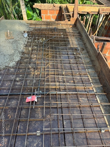 House construction site in Kerala, India, showing a partially built residential home with concrete columns, exposed brick walls, construction materials, and workers’ activity.