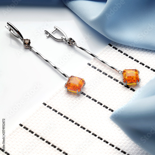 Fotografía Elegant Amber Earrings with Silver Accents Highlighted on a Soft Blue Fabric Sur