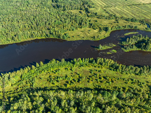 Aerial view of a winding river meandering through green taiga forest and fields near Kindasovo village in Karelia, Russia