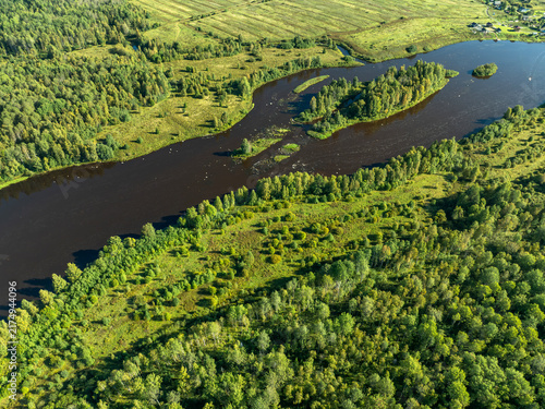 Aerial view of a winding river meandering through green taiga forest and fields near Kindasovo village in Karelia, Russia