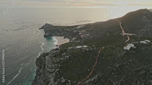 Aerial drone orbit reveals Cape Point coastal trails winding across rugged green cliffs above turquoise coves and open ocean, offering serene travel view of protected shoreline in Western Cape