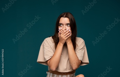 Fotografie Young woman covering mouth with hands, feeling fear, expressing shock, keeping a