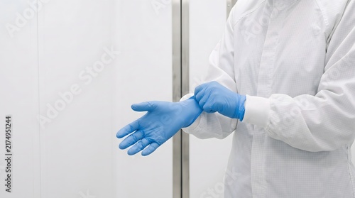 Cleanroom worker pulls a blue nitrile glove cuff securely over a white coverall sleeve, demonstrating contamination-control gowning before precision manufacturing.