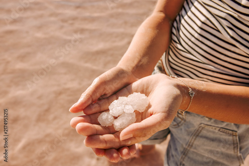 holding natural salt crystals in cupped hands at a sunny lakeshore with close up view of mineral texture and striped summer clothing, concept of wellness, skincare, natural cosmetics
