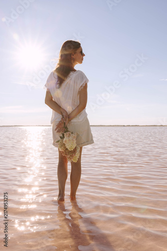 woman in shallow lake with flower bouquet, peaceful waterside during sunny summer evening with glowing reflections, mindfulness, solitude and nature, travel tourism, wellness retreat