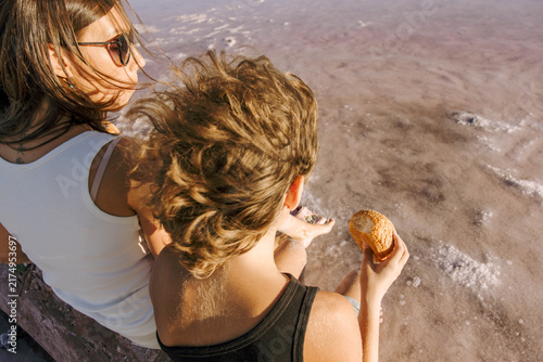mother and child eating fresh bread on driftwood log beside shallow salt lake during warm summer sunset with peaceful family picnic atmosphere concept of family travel, bakery, tourism