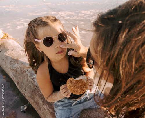 mother caring for daughter and wiping face while child holding sesame bread on driftwood at pink salt lake, family outdoor moment, parenting family care travel lifestyle bakery business