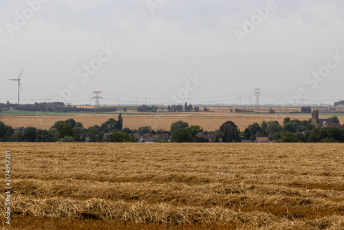 Fotografía Rural village with church tower, wind turbines and power lines beyond a harveste