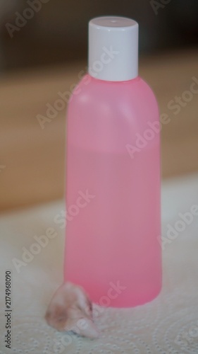 Pink cosmetic bottle stands beside a small piece of cotton on a light surface. The image represents cleansing, preparation, hygiene, and organized personal beauty care.