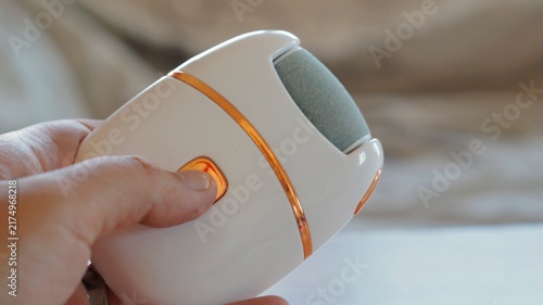 A hand holds and switches on a compact electric foot file for pedicure care. The image represents modern grooming technology, convenience, personal hygiene, and self-care.