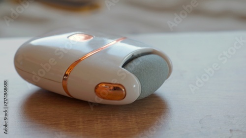 Compact electric pedicure device lies on a soft surface in a close-up product view. The image represents modern personal care, technology, convenience, and beauty routines.