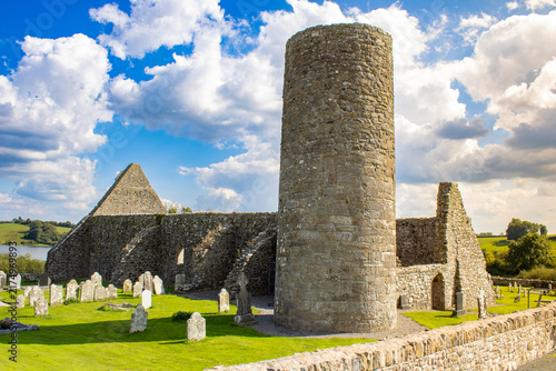 Foto Drumlane Abbey and medieval round tower in County Cavan, Ireland, with historic church ruins, gravestones and dramatic summer clouds beside Garfinny Lough