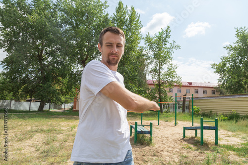 Adult athlete stretches arms beside outdoor workout bars, preparing body for active session. Stretching releases tension, stretching improves range, while stretching content fits wellness media.