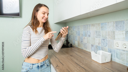 attractive smiling woman in kitchen at home relaxed using smartphone wearing white shirt and jeans