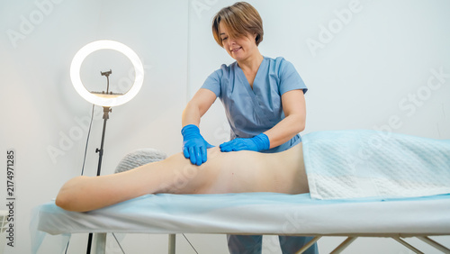 A woman is lying face down on a massage table while a massage therapist is applying pressure to her back in a spa setting, copy space