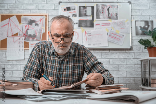 Foto and taking notes in front of a board covered with clues, and mysterious images in the background