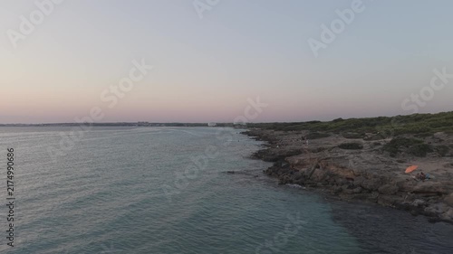 Aerial wide view of Punta della Suina coastline in Gallipoli, Salento, Italy. Drone shot of the turquoise Ionian sea, rocky shore, and pine forest at dusk.