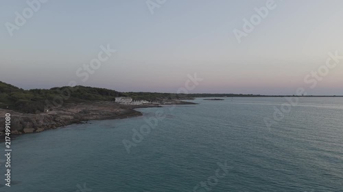 Aerial drone perspective of Punta della Suina beach resort and coastline in Gallipoli, Puglia. Crystal clear turquoise water and Mediterranean scrub at sunset.