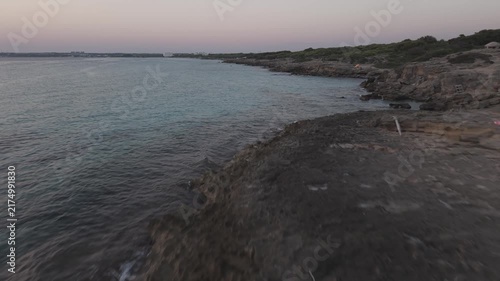 Aerial wide view of Punta della Suina coastline in Gallipoli, Salento, Italy. Drone shot of the turquoise Ionian sea, rocky shore, and pine forest at dusk.