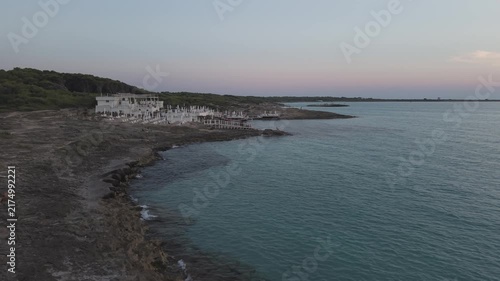 Aerial drone perspective of Punta della Suina beach resort and coastline in Gallipoli, Puglia. Crystal clear turquoise water and Mediterranean scrub at sunset.