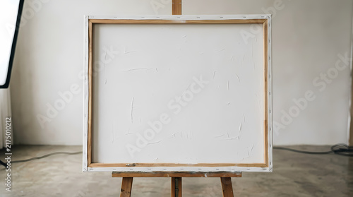 Empty rectangular canvas stretched on wooden frame displayed upon tall tripod stand ready for creative artists to paint their colorful masterpiece ideas with professional heavy oil acrylic