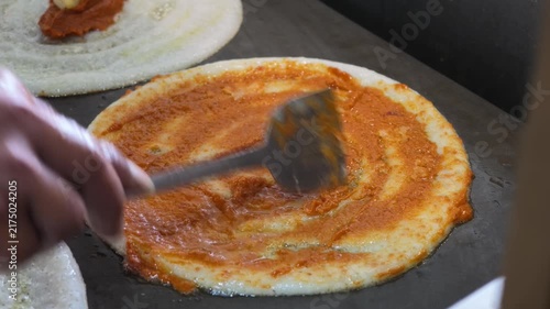 spicy masala being spread over crispy benne dosa on hot griddle
