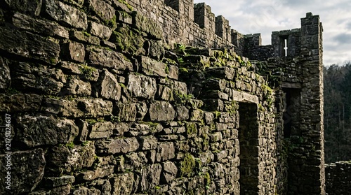 Ancient mossy castle stone wall, stacked irregular rocks with cinematic side lighting casting deep shadows on worn masonry, medieval feel.