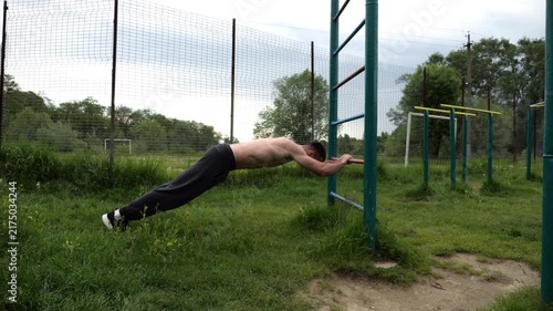 Young muscular athlete doing exercise on triceps at sport equipment outdoor. Male shirtless athlete working out at sport ground. Strong sporty man training at nature. Concept of healthy lifestyle