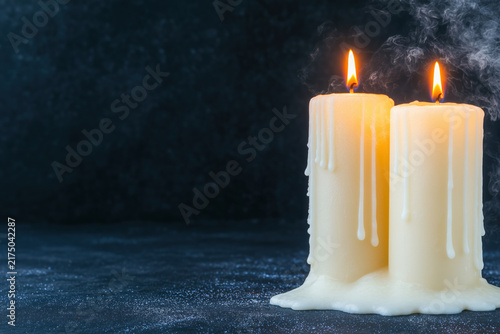 Lit white pillar candle with melting wax on a dark background with copy space.