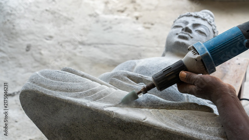 Foto Sculptor using angle grinder to carve reclining Buddha statue from stone traditi