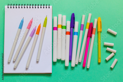 An open spiral notebook with colorful markers arranged across a mint green surface creates a bright workspace for writing, drawing, and creativity.
