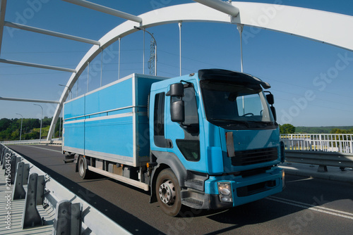 Rigid lorry driving across an arched bridge under a clear blue sky.