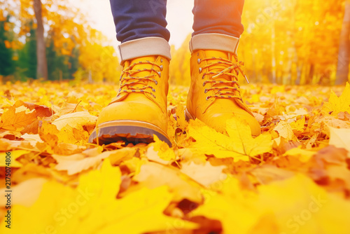 Yellow leather boots walking on fallen autumn leaves background.