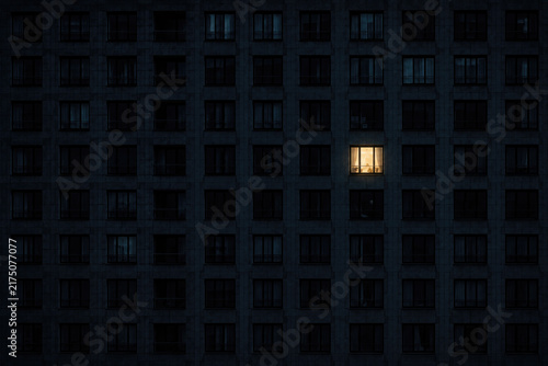 One illuminated window glows in a dark building facade.