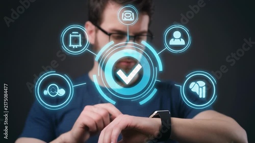 Man checking smartwatch showing digital interface with checkmarks and icons during dark studio lighting