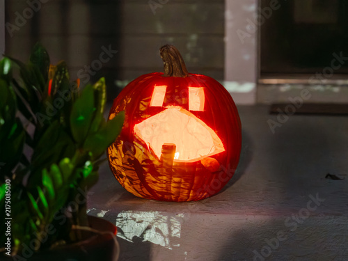 A glowing carved pumpkin lights up a front porch at night. The classic jack o' lantern is a timeless symbol of Halloween celebrations.