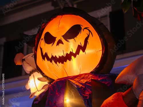 Фотография A glowing inflatable pumpkin character lights up a front yard during Halloween night