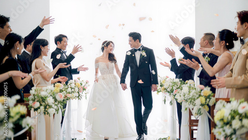 Joyful asian bride and groom walking down the aisle through flower petals as guests cheer, happy wedding recessional moment