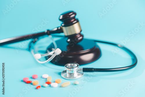 Fotografie Judge gavel, stethoscope, and colorful pills on a blue background represent healthcare law, pharmaceutical regulation, medication safety, malpractice, patient rights, compliance, and justice