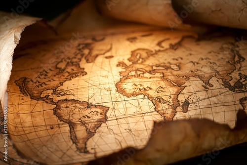Closeup of an original antique world map printed on weathered parchment with faded sepia coastlines hand drawn mountain symbols decorative navigation lines grid pattern curled paper edges illuminated