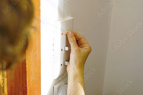 Fotografie Woman turning off indoor lighting at switch panel