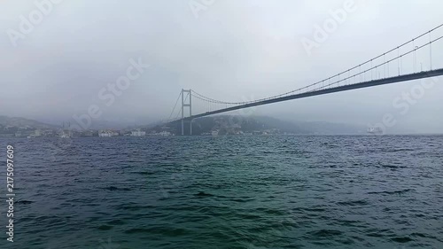 Scenic View of the Bosphorus Bridge Spanning Across Misty Sea Waters on a Foggy Overcast Day with Seagull Flying and Cargo Ship in Distance, Iconic Landmark Cityscape in Istanbul, Turkey