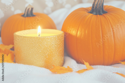 Burning yellow candle with large orange pumpkin on soft light background with copy space.