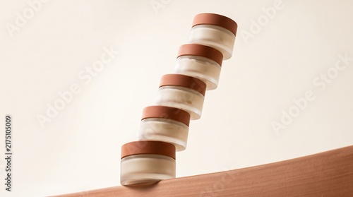 Minimalist skincare product display featuring a gravity-defying stack of five glass cream jars with terracotta colored lids on a wavy textured terracotta surface against a neutral soft beige