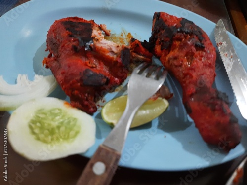 Foto Spicy Red Tandoori Chicken Leg Served with Lime and Cucumber Slices on Blue Plat