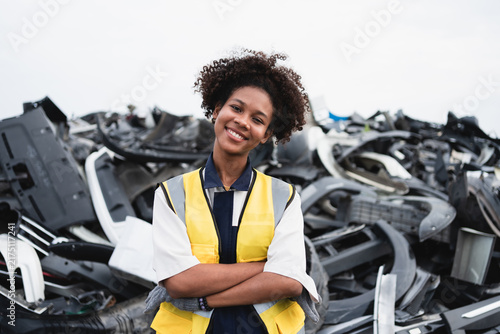 A recycling worker handles a salvaged vehicle component beside a large scrap pile, representing automotive waste recovery and circular economy practices