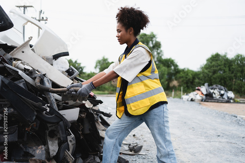 A recycling worker lifts a recovered automotive component in a scrapyard, illustrating hands-on sorting, material recovery, and sustainable waste management